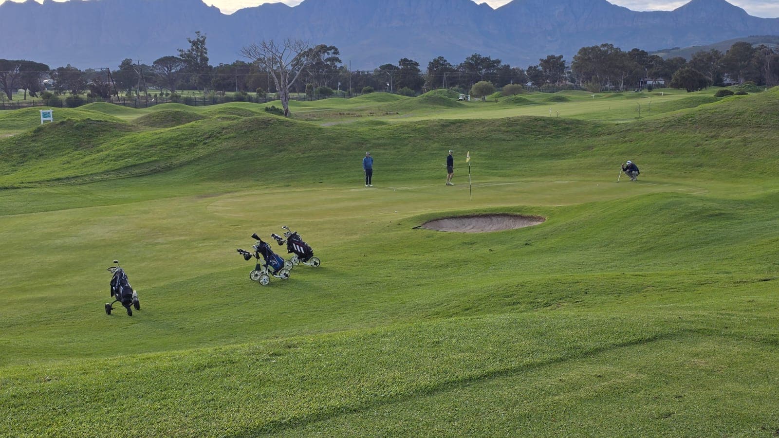 Golfers on a green below the mountains